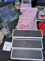 Lot items arranged on a metal surface: Copco shelf organizers, striped napkins, Julep drink books, clear glass, decorative ceramic item.