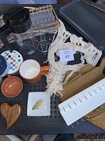 Top view of assorted houseware items including mugs, macrame cup holder, wooden and ceramic dishes, metal drying rack, plastic pitcher, and beige apron.