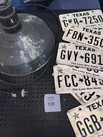 Photo showing industrial metal light fixture base and multiple Texas license plates laid out on a black perforated surface