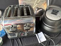 Delonghi four-slot chrome toaster and Instant Pot Air Fryer Lid 6 shown side by side on black fabric, with lot tag 47