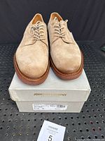 Front view of the shoes placed on top of the original Johnston & Murphy shoebox showing taupe suede uppers and plain toe design.
