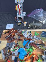 Assorted Lego castle parts spread on cutting board including brown, blue, green pieces plus Lego animal figures in front