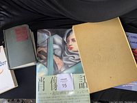 Shows three books: Tamara de Lempicka art book with Japanese text cover wrap, beige hardcover with fish embossing, and small gray-green hardcover book.