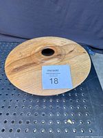 Carved magnolia wood burl bowl with visible grain and knot patterns, circular shape with small hole in the center. Shot taken on perforated black surface showing residue marks on top surface.