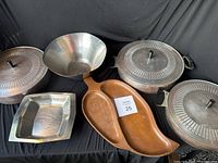 Full set of mid century Presto Ware metal cookware and serving pieces on black fabric background showing lidded pots, rectangular pan, bowl, and divided dish.