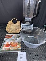 Shot of the lot showing the Ninja blender, clear glass bowl with spout, straw basket, and Julep book arranged on a perforated surface with black backdrop.