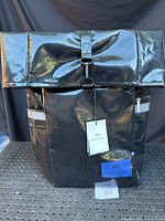 Front view of black PVC backpack with fold-over top and PS tag attached