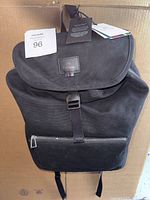 Front view of black canvas Paul Smith backpack showing flap with buckle closure, front zip pocket, and logo label.
