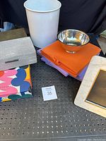 Photo showing fabric storage boxes, small white trashcan, puzzle box sealed, metal bowl, and folded fabric