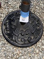 Close-up image of the round ornate cast iron base with floral and swirl pattern and central pipe wrapped with blue tape and label 54.