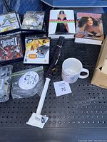 PlayStation 2 game cases stacked with a couple books, a white mug, cleaning wipes, and cleaning tools on a black surface