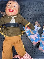 Photo showing full Davy Crockett plush doll with plastic face wearing brown outfit and coonskin cap beside collectible badges and clicker toys in original packages.