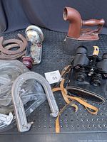 Vintage iron, Tasco binoculars, plastic horseshoes, and metal horseshoes arranged on a black surface