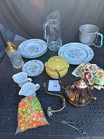 Wide shot showing all kitchen items including plates, pitcher, teapot, glass container, metal cup, copper kettle, and bagged cupcake decorations.