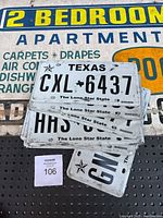 Photo showing vintage painted plywood sign advertising 2 bedroom apartment with various features listed, and a stack of Texas license plates on top.