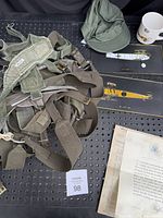 Top view of olive drab military suspenders, green military cap, two model airplane ribbon displays, military mug, and documents including Truman letter and officer directory.