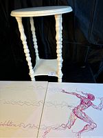 White spindle leg wooden end table shown from an angle with the running man artwork on the floor in front of it.