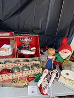 Photo showing a box with sets of Christmas ornaments including a Santa Claus head, reindeer, angel topper, elf, and two white angel ornaments with ribbons.