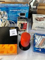View of various boxed electronics including the Polaroid Portable DVD Player PDV-0700 with cables, personal alarm, red Paterson darkroom light, and Smartphone Projector box partially visible.