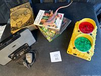 Lot display showing Altec Lansing stereo dock, stacked XBOX 360 games, faux book with pet lizard figure, and traffic light decorative item.