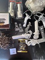 Variety of flag holders, power strip, boxed powered post cap, string lights wiring, hardware brackets, and gloves in a mesh bag together on table.