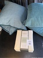 Full view of the organic sheet set packaging and four blue textured throw pillows on a black surface.