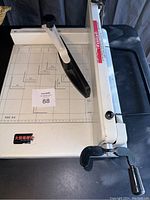 Top left view of the paper cutter showing the cutting base with measurement grid and the handle arm with black grip.