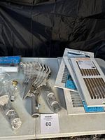 Full view of assorted ventilations grates, light bulbs, flag brackets, outlet covers, and small hardware placed in a box on a white table with black background.