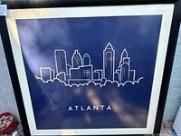 Front view of the framed Atlanta skyline print showing the navy blue background and white line drawing with some natural reflections and shadows.
