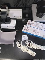 Collection of desk organizing supplies including nested storage boxes, black cylindrical containers, power strips, and boxed tripod easel.