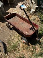 Full view of the red metal wagon showing wear, red paint, handle and bed.