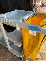 Gray Rubbermaid janitorial cart showing multiple shelves and yellow removabe trash bag holder.