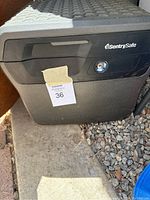 Black SentrySafe locking safe on concrete and gravel ground, showing front panel and key lock.