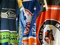 Four sports flags displayed partially folded showing team logos including Seattle Seahawks, Golden State Warriors, New York Yankees/Mets combo flag