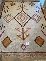 Full view of the cream-colored shag Moroccan rug with colorful geometric diamond and arrow patterns and fringe ends.