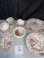 Full vintage china set with plates, teacups, and bowls arranged on table showing floral patterns and overall quantity.