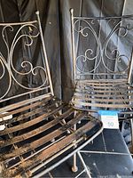 Pair of vintage wrought iron folding patio chairs showing detailed scrollwork on the backrests and metal slat seats.