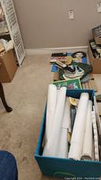 View of blue storage bin with multiple rolled white papers and some loose papers on floor