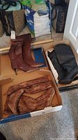 Three pairs of women's calf boots placed in shoeboxes on carpet. Includes dark brown faux crocodile leather boots, black boots, and light brown faux snakeskin boots.