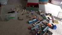 Wide photo showing a large assortment of jewelry pieces spread on the floor including necklaces, brooches, pins, and bracelets, many organized in boxes and trays.