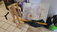 Overall view of the wooden easel and two floral canvases with white orchid paintings placed against a wall.