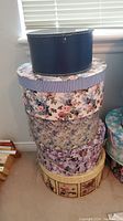 Stack of five decorative hat boxes with floral and striped patterns, various colors and designs.