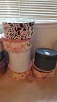 Stack of six decorative hat boxes with various patterns: black and white animal print, pink floral, checkered white, multi-color polka dots, black and beige with ribbon.