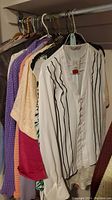 Photo showing several women's blouses and jackets hanging on hanger, including white blouse with black stripes and cream lace blouse