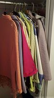 Closet view of various lady's tops, blouses and jackets on hangers, showing assorted colors and fabrics.