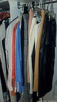 Wide view of skirts and tops hanging on a rod. Includes multiple colors and styles, primarily skirts being tan, cream, black, beige and several tops in different colors.
