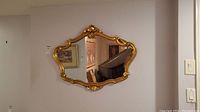 Front view of the gold framed wall mirror hanging on a white wall with visible room background.