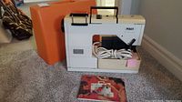 Pfaff sewing machine mounted with power cord and foot pedal in front, manual on floor, orange case behind