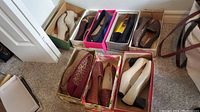 Photo showing 8 pairs of women's flats and low heel shoes in various colors, some in shoe boxes on carpeted floor.