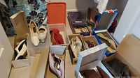 Overview of multiple pairs of women's shoes and ankle boots in boxes, various styles and colors, showing the full lot